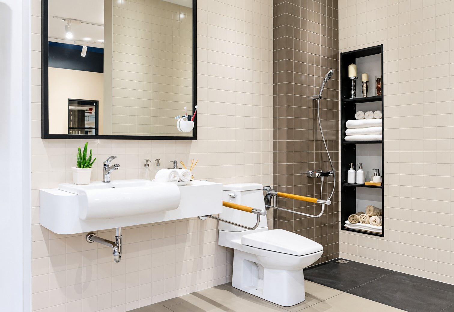 Salle de bain moderne aux carreaux beiges avec lavabo suspendu, toilettes équipées de barres d'appui en bois et douche de plain-pied.