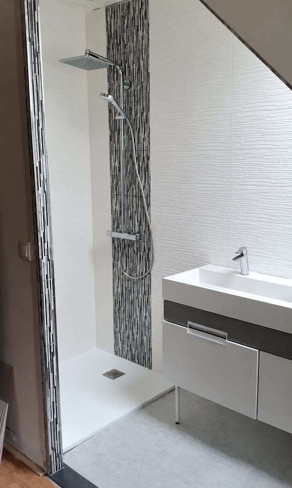 Salle de bain sous pente récemment rénovée, avec une douche à l'italienne dotée d'une bande de mosaïque noire et blanche, et un meuble vasque blanc suspendu.
